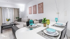 Ein modernes Wohnzimmer mit Essbereich, ausgestattet mit einer Couch, einem Couchtisch, einem Esstisch mit blau-weißen Schüsseln und einem Blumentopf.