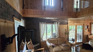 Interior acogedor de una cabaña con chimenea, muebles de madera y una zona en el entrepiso.