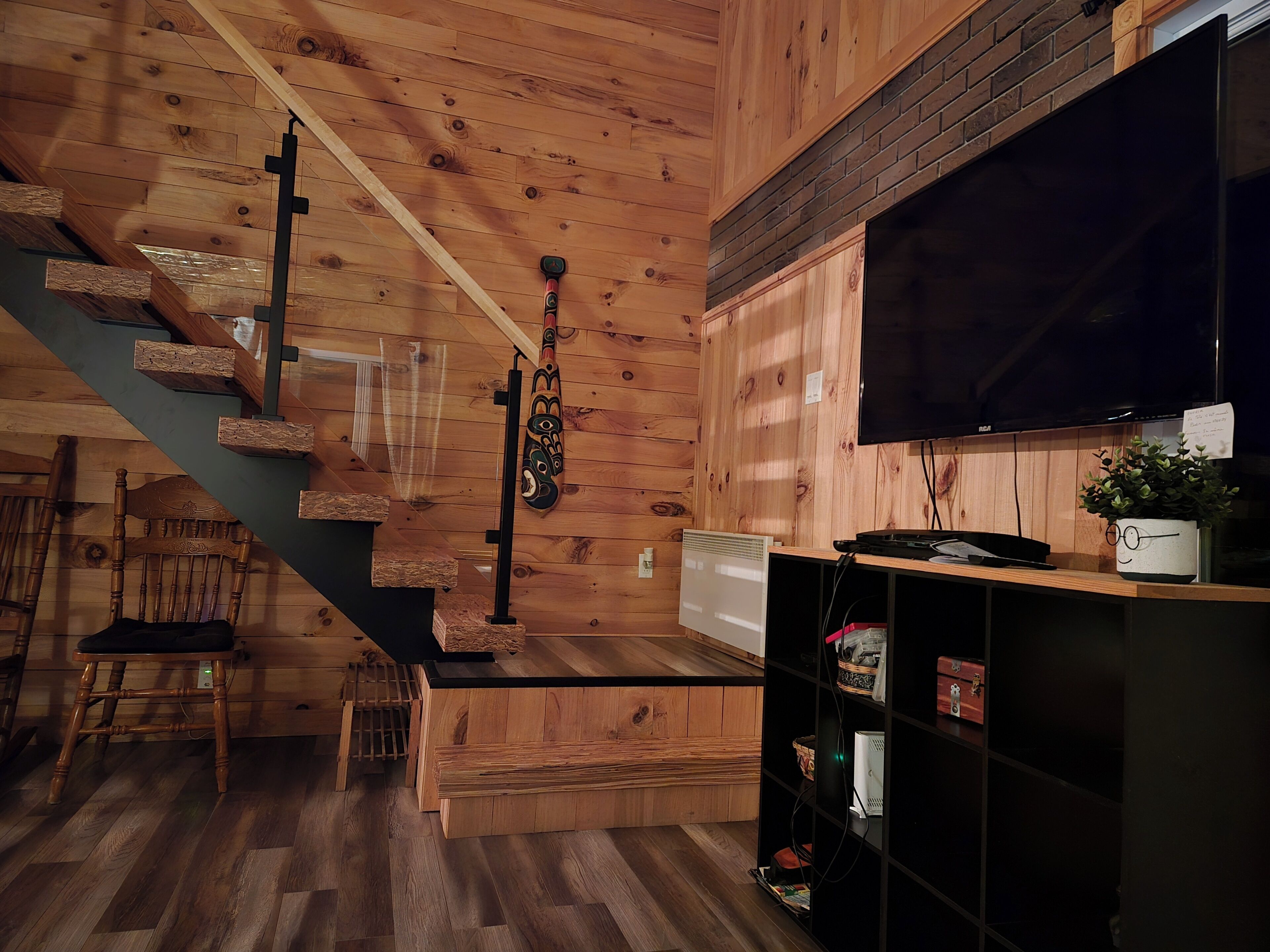 A wooden interior with a staircase, a TV, and a shelf with items.