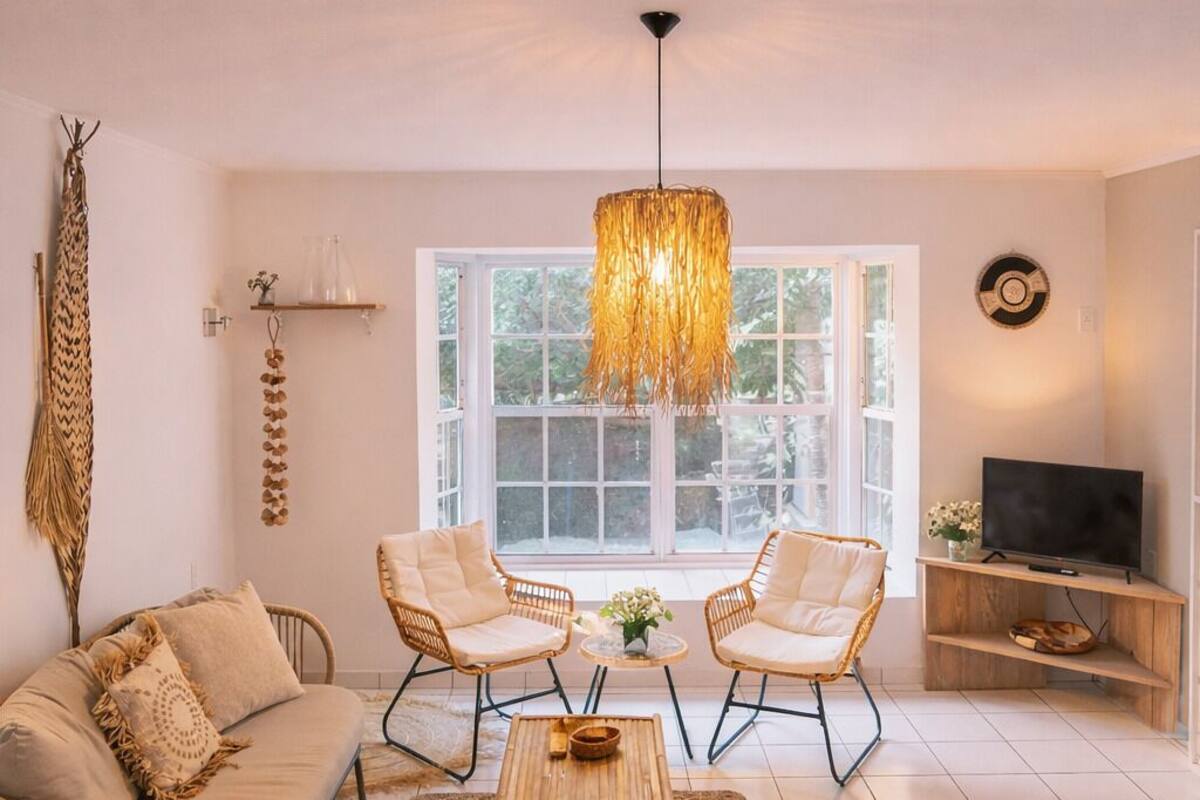 Un salon comprenant un canapé, deux fauteuils, une table basse, un téléviseur posé sur un meuble en bois et une grande fenêtre.