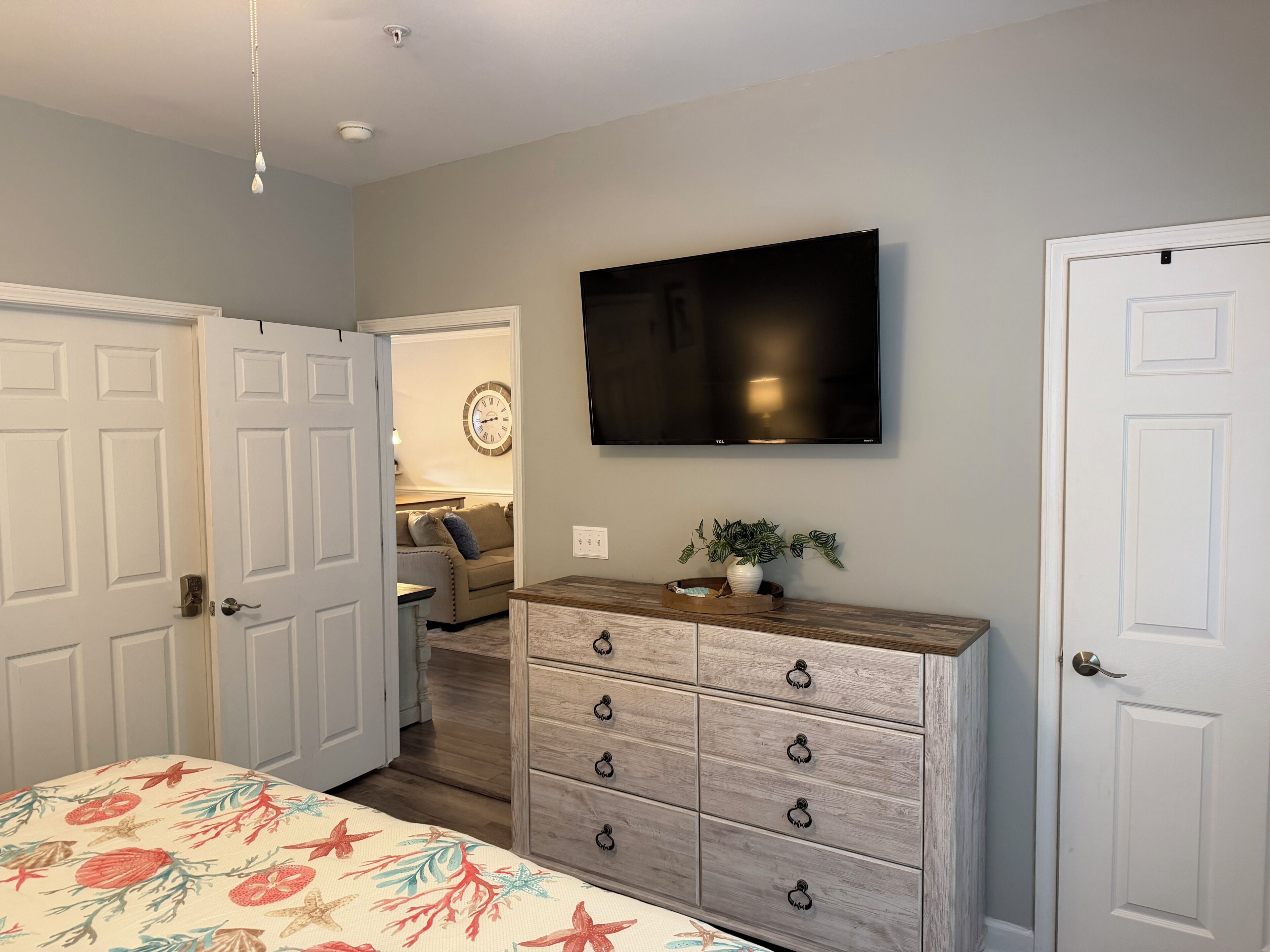 A bedroom with a bed, dresser, TV, and a door.