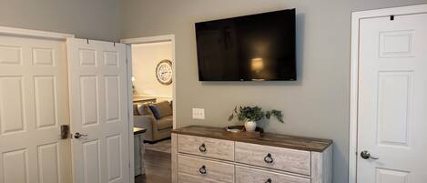 A bedroom with a bed, dresser, TV, and a door.