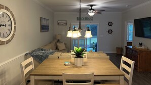 Een eetgedeelte met een houten tafel, stoelen, een plafondventilator en een wandklok.