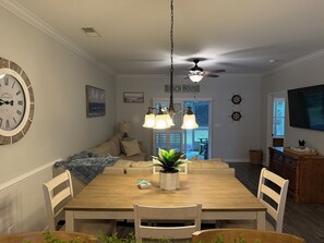 Een eetgedeelte met een houten tafel, stoelen, een plafondventilator en een wandklok.