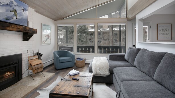 A modern living room with a fireplace, a large gray sofa, a blue armchair, and a wooden coffee table. - 929 Red Sandstone 3 Bedroom Condo (Vail)