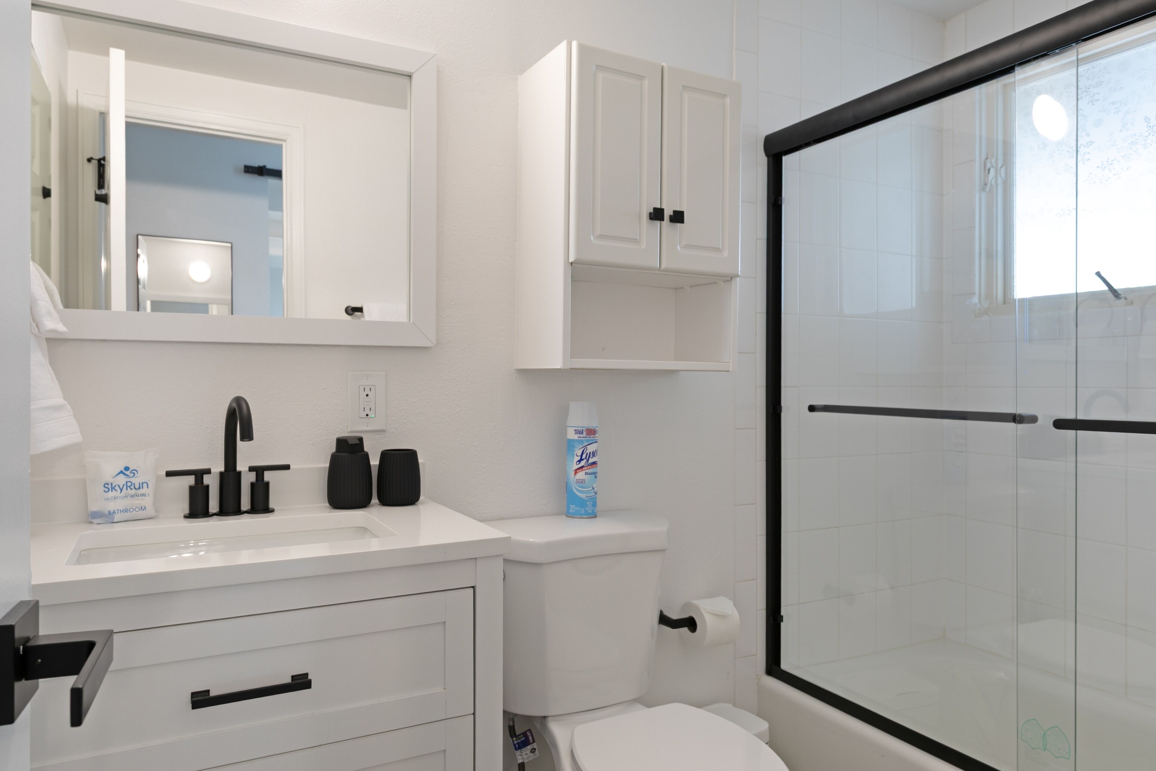 A modern bathroom with a white sink, black faucet, and a glass shower enclosure.