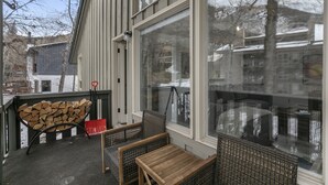 A covered outdoor seating area with a firewood stack, wicker furniture, and large windows. - 929 Red Sandstone 3 Bedroom Condo (Vail)