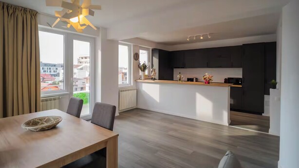 A modern kitchen with dark cabinets, a central island, and a dining area with a wooden table and chairs. - Penthouse with Rooftop next to the Park (București)