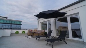 A rooftop terrace with outdoor furniture, including a sofa and lounge chairs, and a large umbrella. - Penthouse with Rooftop next to the Park (București)
