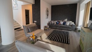 A modern living room with a grey sofa, a coffee table with drinks, a striped rug, and a staircase in the background. - Penthouse with Rooftop next to the Park (București)