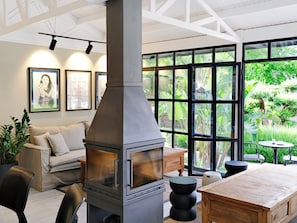 A modern living room with a large fireplace, comfortable seating, and large windows offering a view of greenery. -  Spacious Family-Friendly 2BR apartment in Bodrum. (Bodrum)