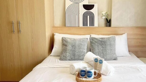 A neatly made bed with pillows, a tray with mugs, and a framed abstract artwork above it. - Room-stylish Studio Stay at Saint Domini (Iloilo)