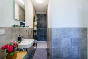 Une salle de bain avec un lavabo, un miroir, une douche et un petit tapis.