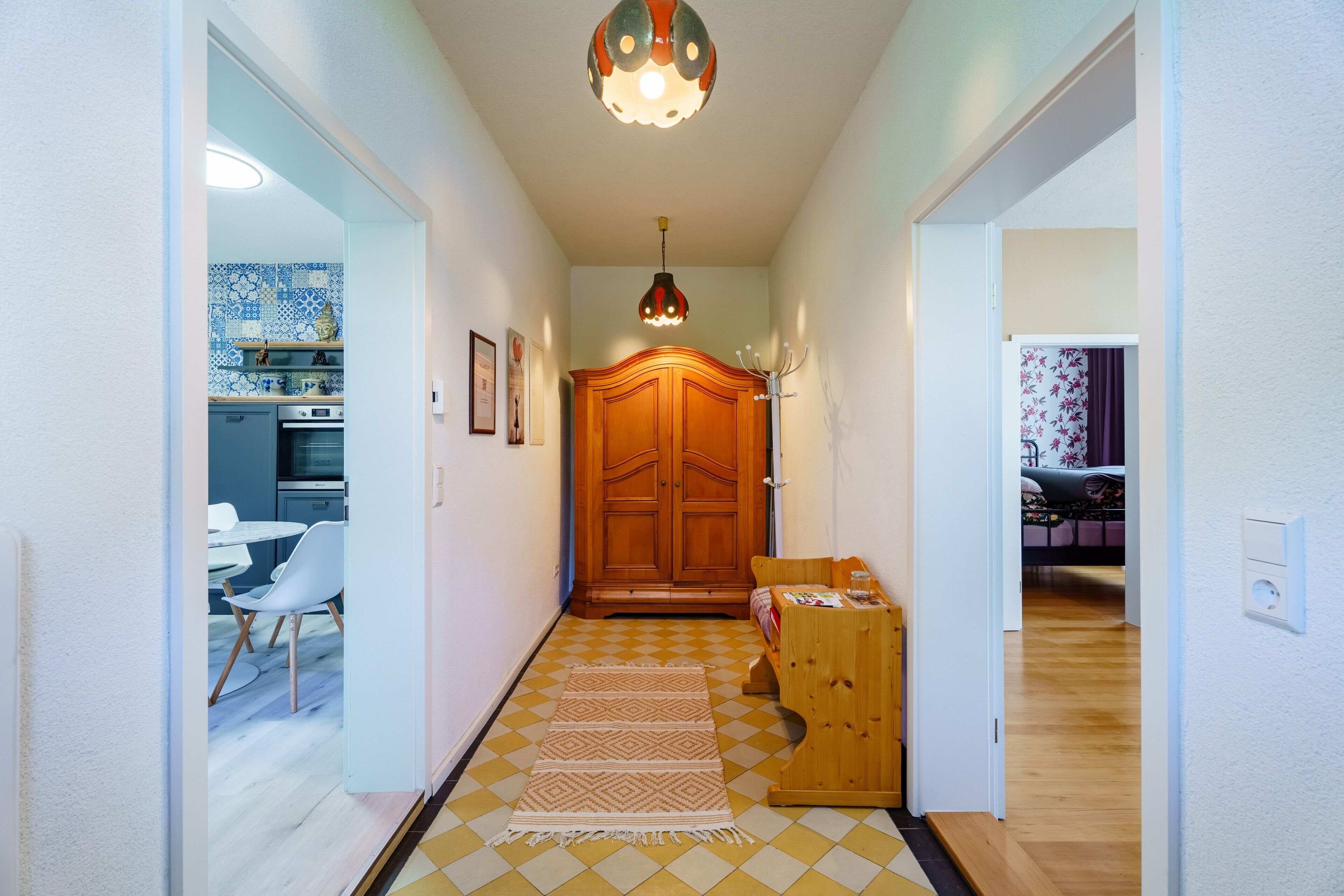 A hallway with a patterned floor, a wooden door, and a dining area with chairs and a table.