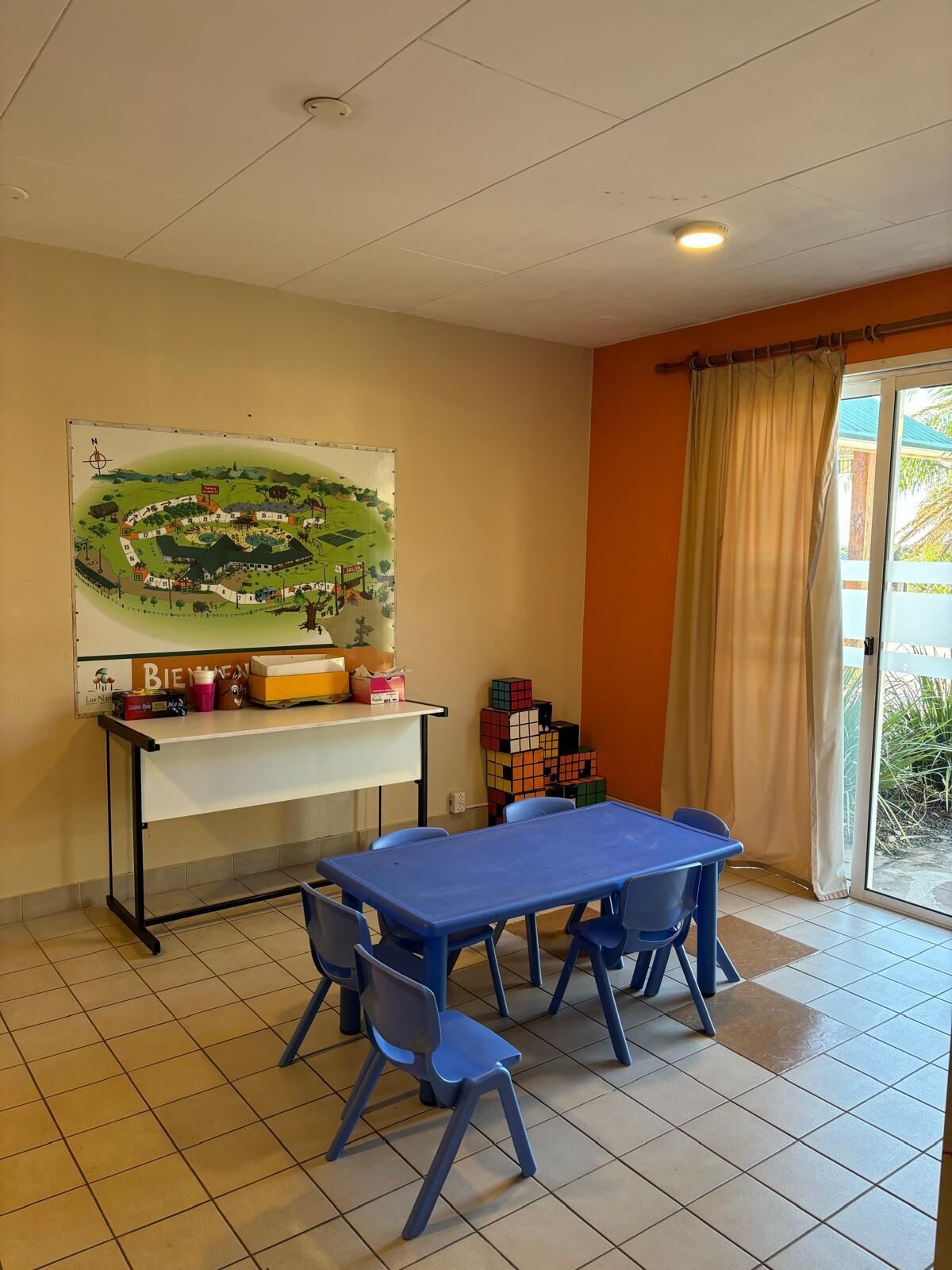 Una habitación con una mesa y sillas azules, un mapa en la pared y una ventana con cortinas.