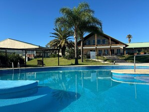A swimming pool with a covered area, palm trees, and a building with a green roof. - Los Naranjos Hotel (Dayman)
