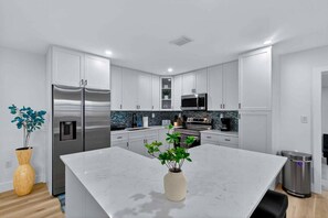 A modern kitchen with white cabinetry, stainless steel appliances, and a marble island. - Serenity Grove 3BR|2BA - Free Parking - Tropical (Miami)