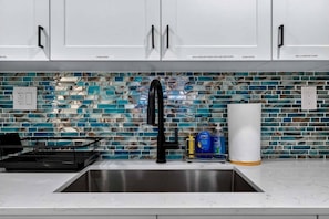 A kitchen with white cabinets, a stainless steel sink, and a backsplash with blue and white tiles. - Modern and Spacious 3BR - 2BA Miami - Free Parking (Miami)