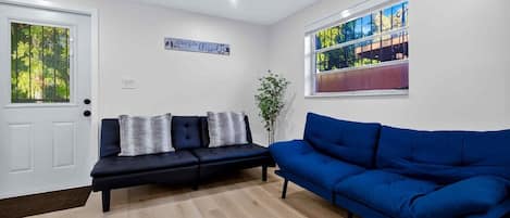 A living room with a dark blue sofa, a white door, and a window with a view of trees.