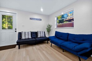 A living room with a dark blue sofa, a white door, and a window with a view of trees. - Modern and Spacious 3BR - 2BA Miami - Free Parking (Miami)
