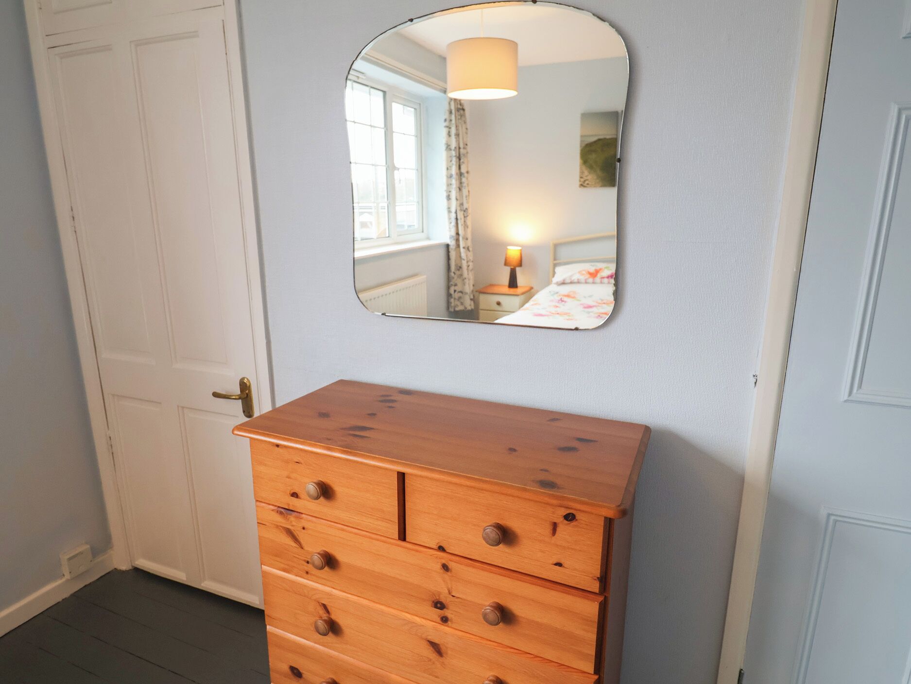 A wooden dresser with drawers and a mirror above it, against a light blue wall.