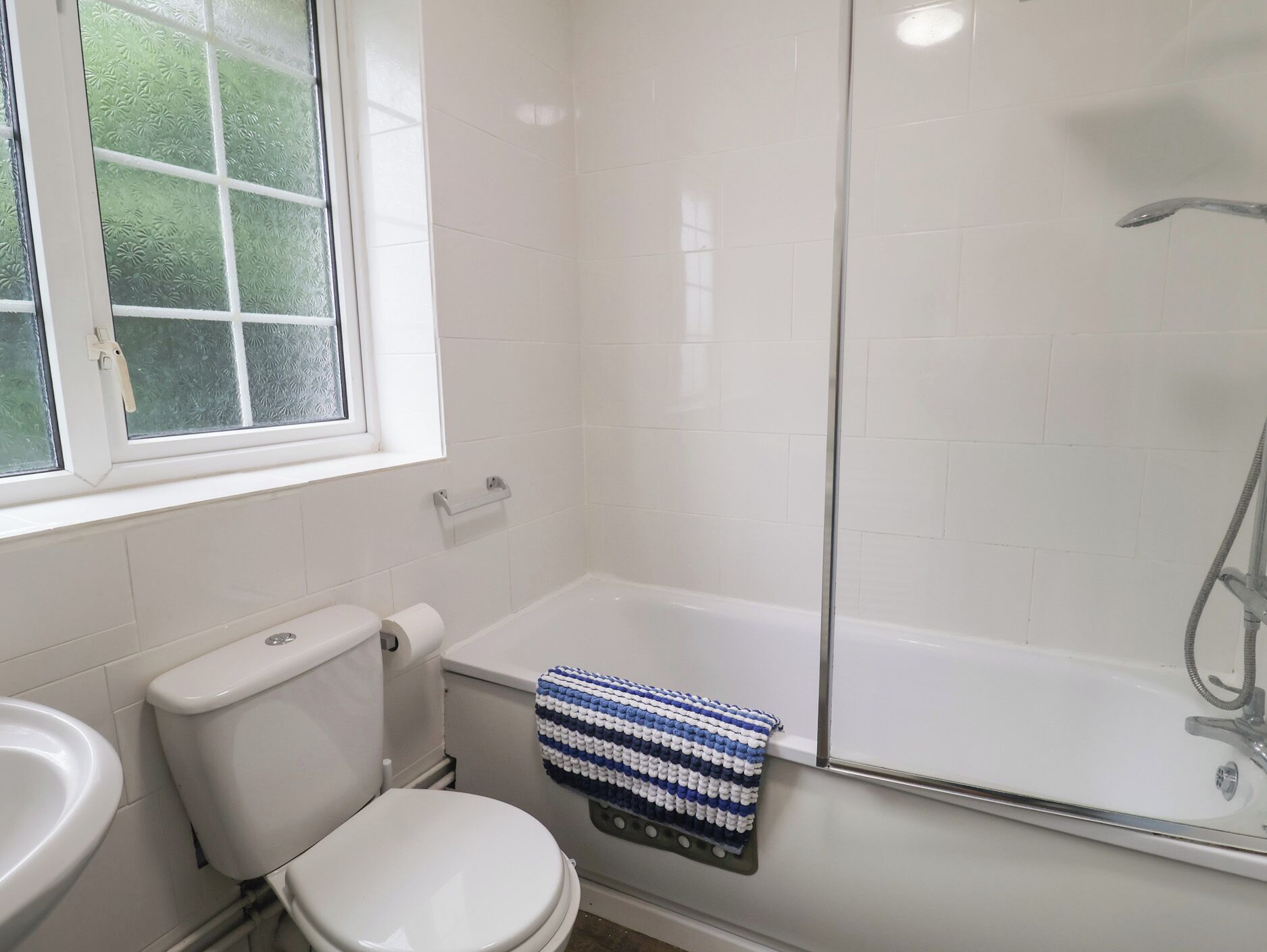 A bathroom with a toilet, a sink, a shower, and a window.