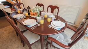 A dining table set for breakfast with plates, cutlery, glasses, and a vase of flowers. - Cromer Holiday Home (Cromer)