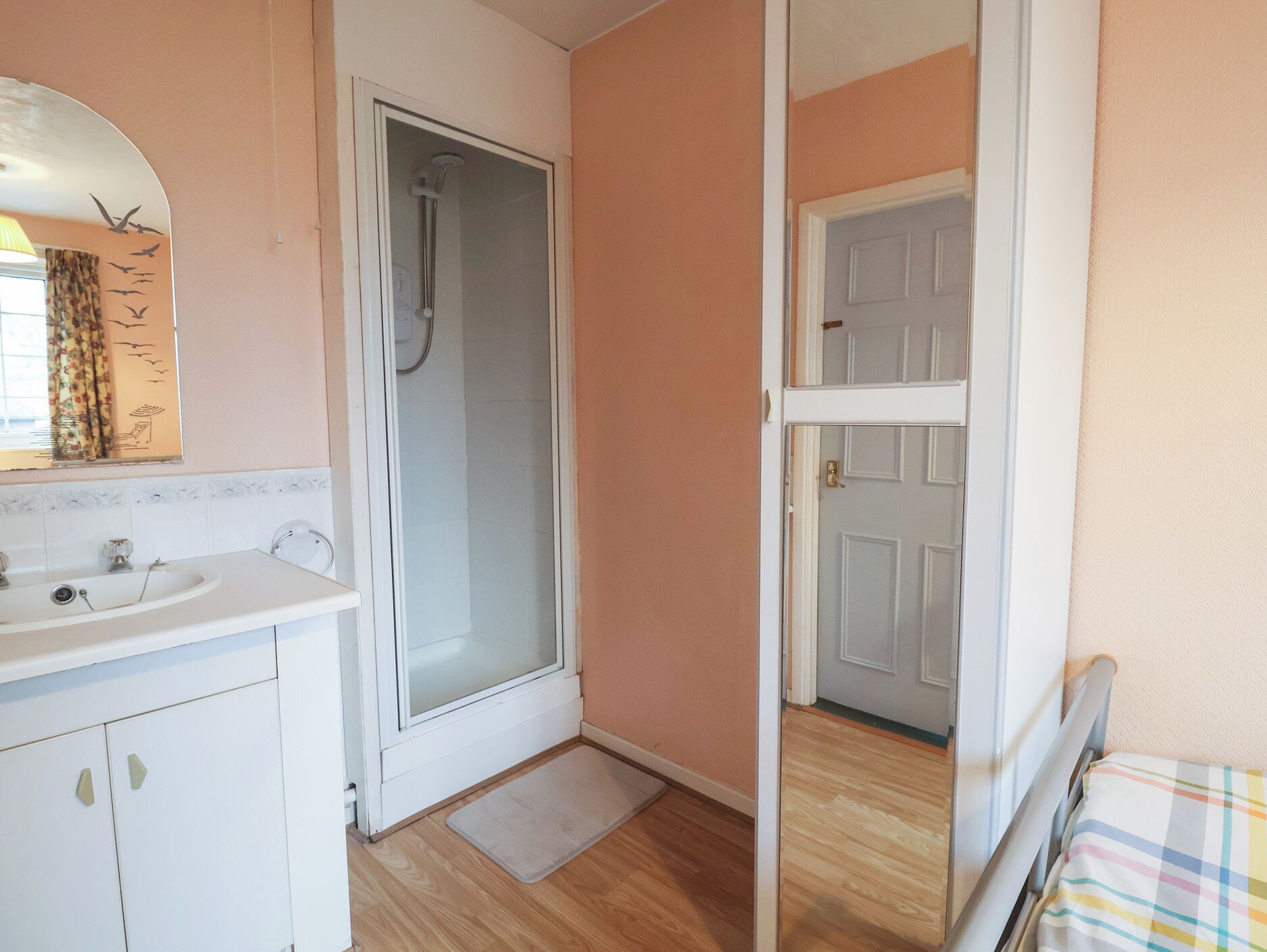 A bathroom with a shower, sink, and a door leading to another room.