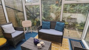 A sunroom with wicker furniture, a blue carpet, and a view of greenery outside. - Cromer Holiday Home (Cromer)