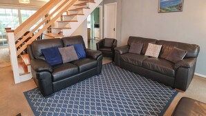 A living room with two black leather sofas, a patterned rug, a wooden staircase, and a painting on the wall. - Cromer Holiday Home (Cromer)