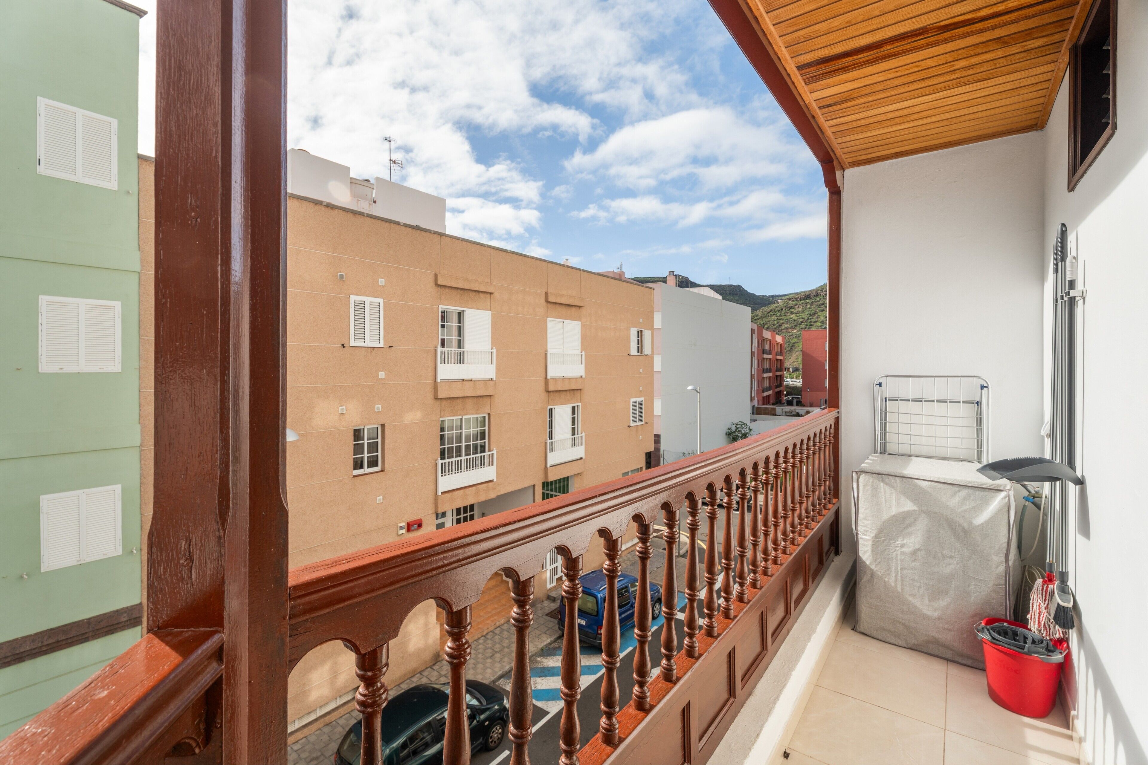 Un balcón con barandilla de madera, un cubo rojo y una zona exterior cubierta.