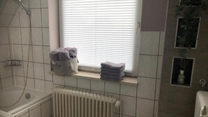 A bathroom with a bathtub, toilet, radiator, and a window with blinds. - Apartment "Wohnung mit Fernblick" with Private Garden and Wi-Fi (Jübek)