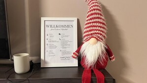 A gnome figurine next to a welcome sign with text in German, a white mug, and a dark wooden surface. - Apartment "Wohnung mit Fernblick" with Private Garden and Wi-Fi (Jübek)