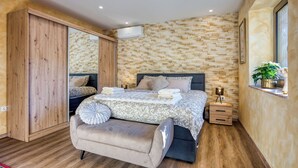 Een slaapkamer met een groot bed, een houten garderobe, een nachtkastje met een lamp en een raam met een plant.