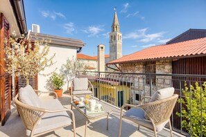 A balcony with wicker furniture, a table with breakfast items, and a view of a church tower. - Vila Leonarda (Miren-Kostanjevica)