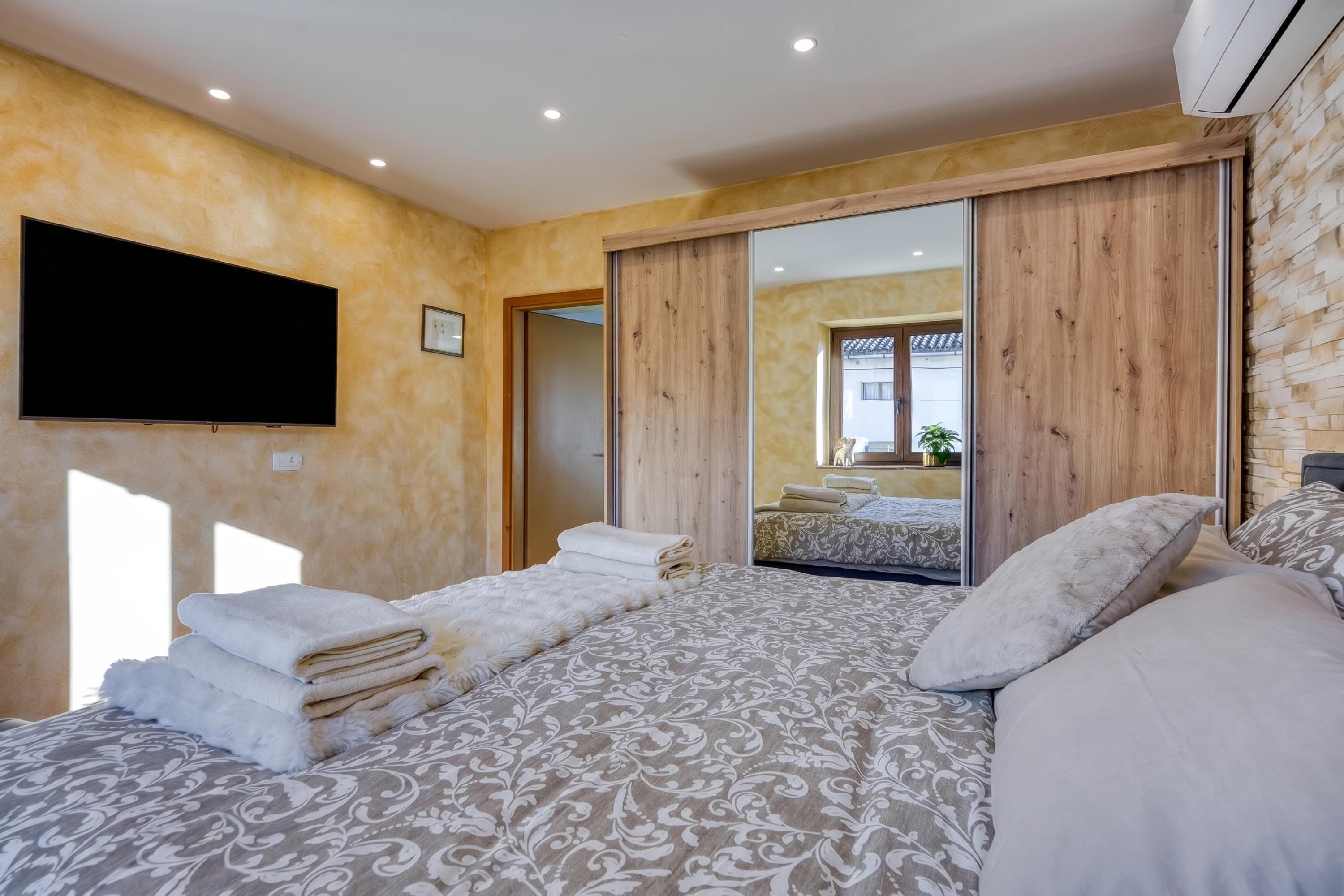 Ein Schlafzimmer mit einem großen Bett, einem flachbildfernseher an der Wand und einer Schiebetür zu einem weiteren Raum.