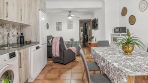 A compact kitchen with a washing machine, a dining area with a table and chairs, and a living area with a sofa and a ceiling fan. - Apartment 'Mi Ilusión' with Wi-Fi (Grazalema)