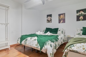 Une chambre avec deux lits, une armoire blanche, une fenêtre et des œuvres d’art murales.