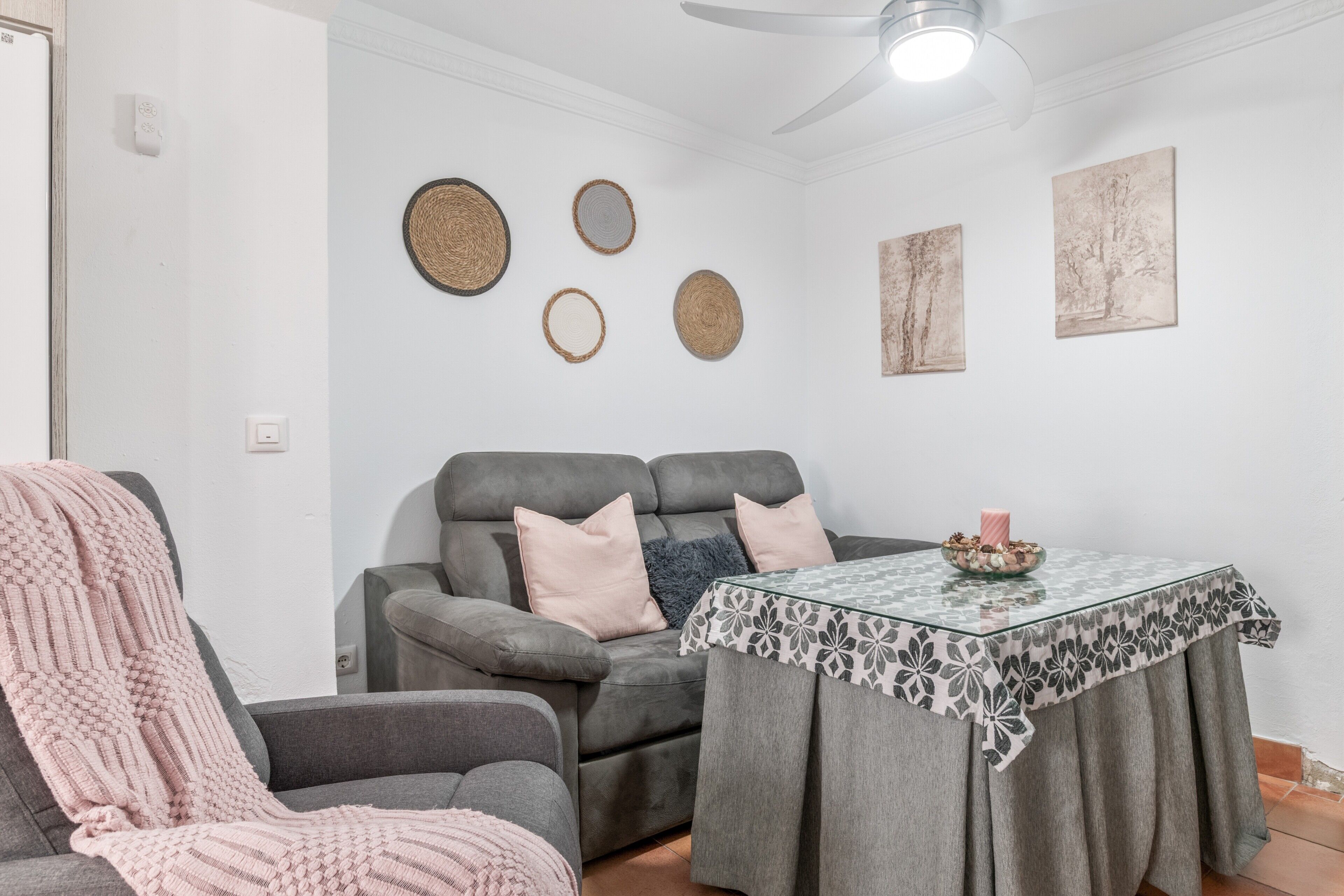 Un salon avec un canapé gris, une table en verre recouverte d’une nappe à motifs et des œuvres d’art accrochées au mur.