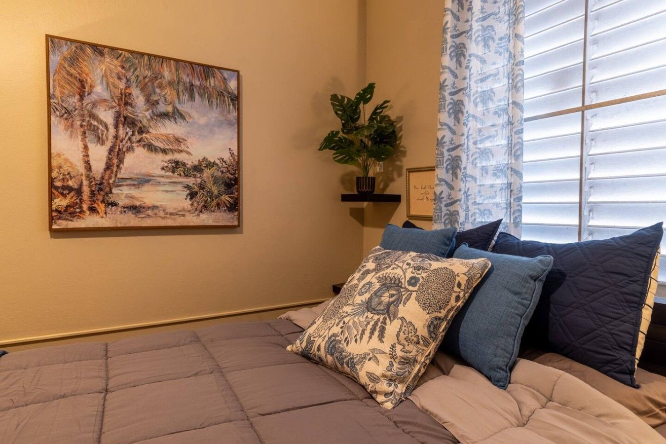 Un dormitorio con cama, un cuadro, una planta y una ventana con persianas.