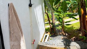 Zona de ducha con una toalla colgada en la pared, cabezal de ducha y un escalón que conduce a un suelo de baldosas.