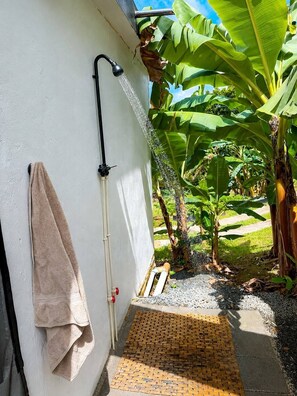 A shower area with a towel hanging on the wall, a showerhead, and a small step leading to a tiled floor. - Coqui Haven Hideaway Rainforest View (luquillo)