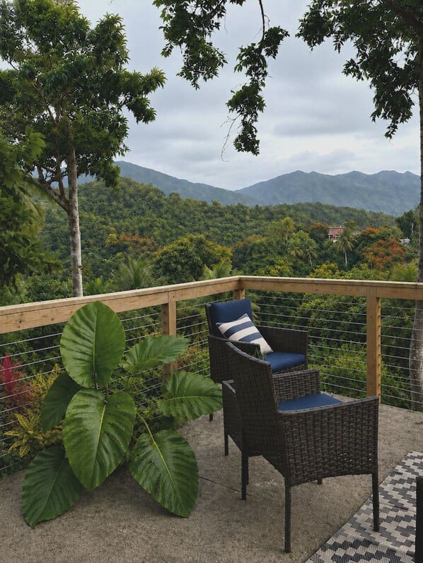 Un balcón con mobiliario de mimbre y vistas a un paisaje montañoso.