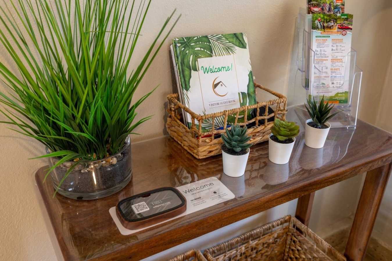 Un mostrador de recepción con un cartel de bienvenida, un libro de visitas, un mapa y plantas en macetas.