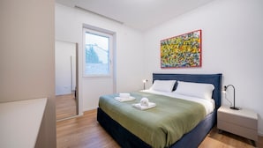 A modern bedroom with a bed, a nightstand, a painting, and a window. - GuestHost - Cozy 60 sqm apartment, located on the first floor of a building without an elevator.The accommodation is situated in a strategic location, allowing you to reach the main points of interest within a short walking distance or by public transpor (Udine)