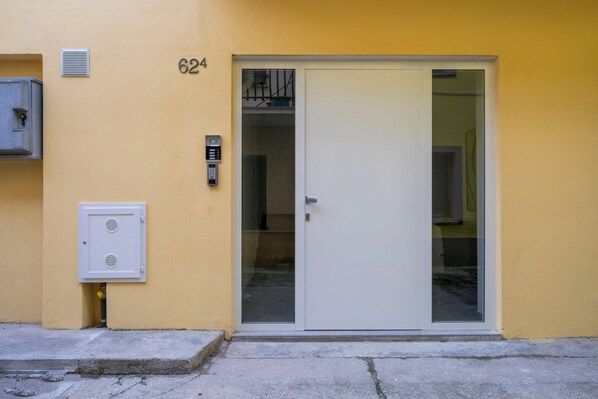 A yellow building with a white door, a keypad, and a small vent.