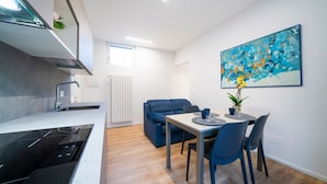 A modern kitchen with a built-in stove, a dining area with a table and chairs, a blue sofa, and a painting on the wall. - GuestHost - Cozy 60 sqm apartment, located on the first floor of a building without an elevator.The accommodation is situated in a strategic location, allowing you to reach the main points of interest within a short walking distance or by public transpor (Udine)