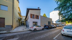 A street with parked cars, a building with a white facade and brown shutters, and a clear sky. - GuestHost - Cozy 60 sqm apartment, located on the first floor of a building without an elevator.The accommodation is situated in a strategic location, allowing you to reach the main points of interest within a short walking distance or by public transpor (Udine)