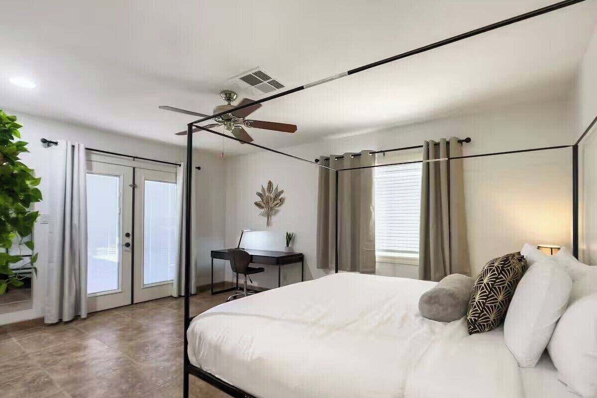 A modern bedroom with a four-poster bed, a desk, and a ceiling fan.