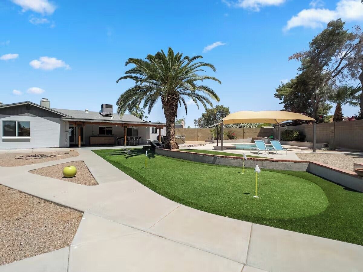 A backyard with artificial grass, a pool, and a covered seating area.